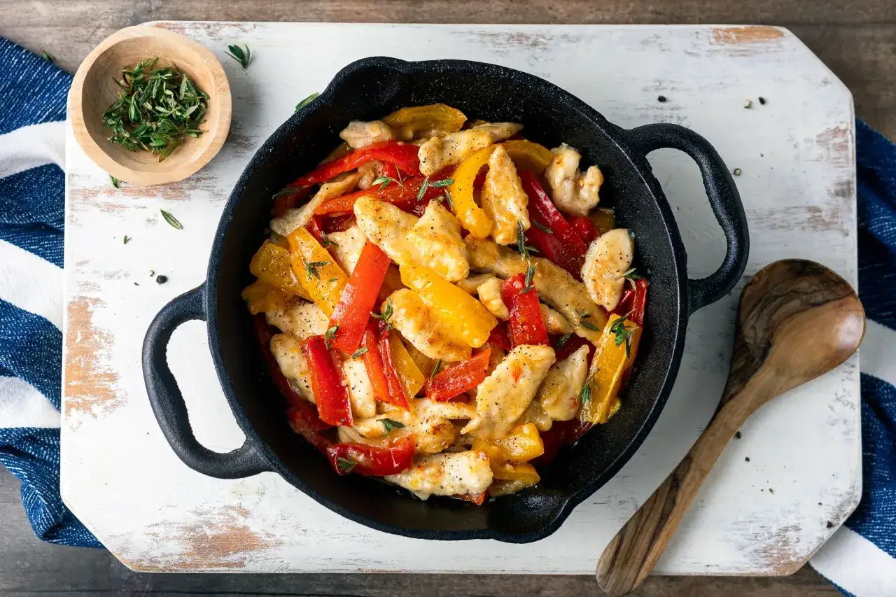 Straccetti di pollo con peperoni rossi e gialli, conditi con erbe aromatiche, serviti in padella.