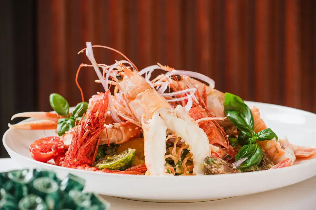 Un'appetitosa catalana di crostacei, con gamberi, scampi, pomodorini e basilico fresco, servita su un piatto bianco.
