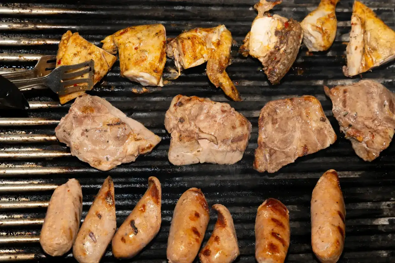 Grigliata di carne con pollo, salsicce e bistecche che sfrigolano sulla griglia.