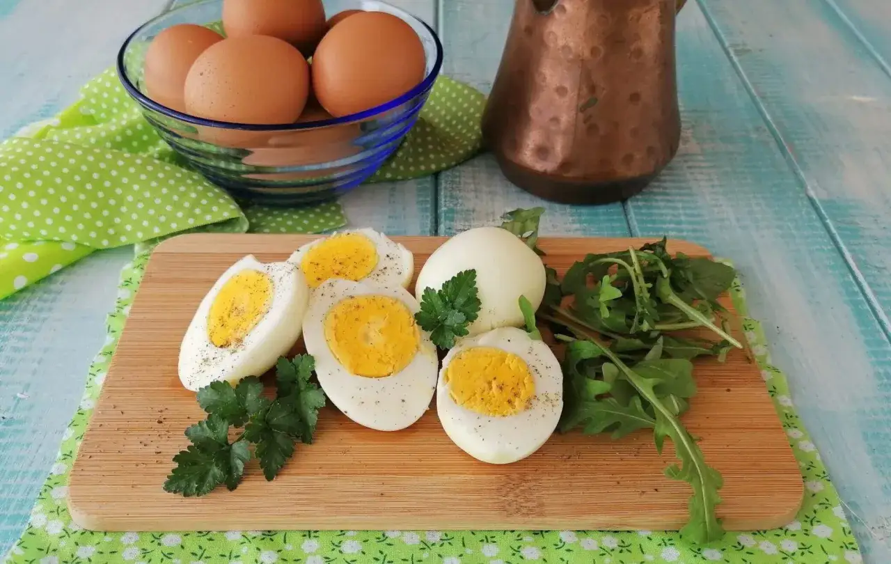 Uova sode in friggitrice ad aria, tagliate a met&agrave;, con un ciuffo di prezzemolo e rucola. Sullo sfondo, uova intere in una ciotola.