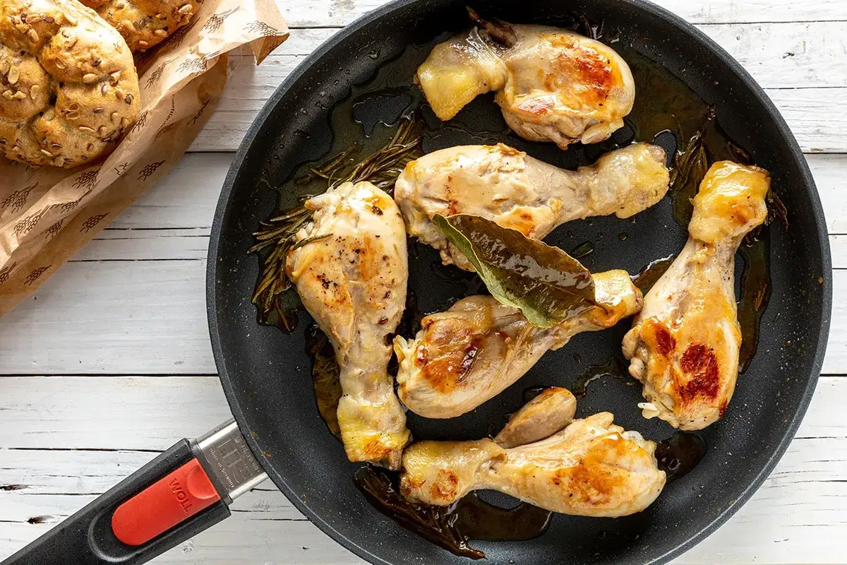 Fusi di pollo succulenti in padella, dorati e profumati con rosmarino e alloro, pronti per essere gustati.