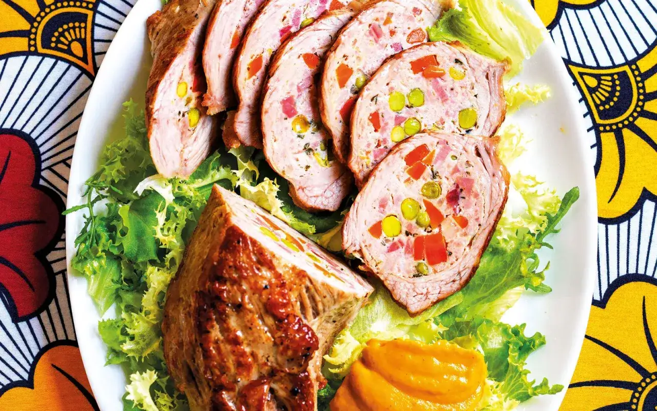 Fettina di carne ripiena con piselli, carote e prosciutto, servita su un letto di insalata verde con una salsa arancione.