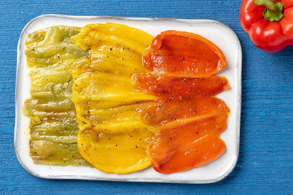 Peperoni verdi, gialli e rossi cotti in friggitrice ad aria, conditi con olio e pepe, su un piatto bianco.