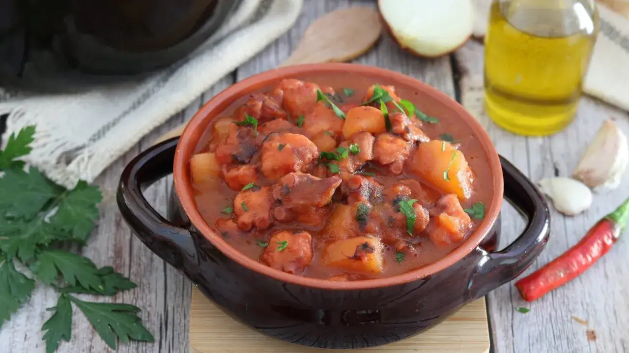 Un saporito polpo alla pignata, con patate e prezzemolo, servito in una ciotola di terracotta. Ingredienti freschi come aglio, peperoncino e olio d'oliva completano la scena.