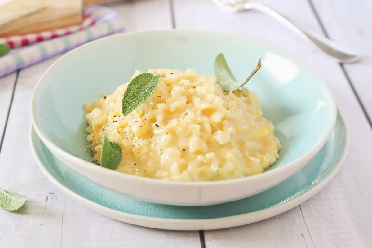 Cremoso riso in cagnone, guarnito con foglie di salvia fresca e pepe nero, servito in una ciotola azzurra.