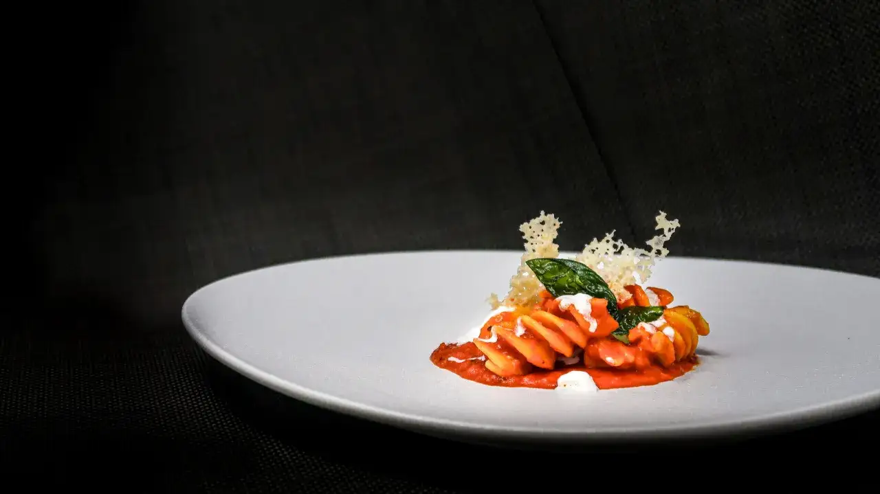 Fusilli al pomodoro con stracciatella cremosa, guarniti con foglie di basilico e croccante di parmigiano.