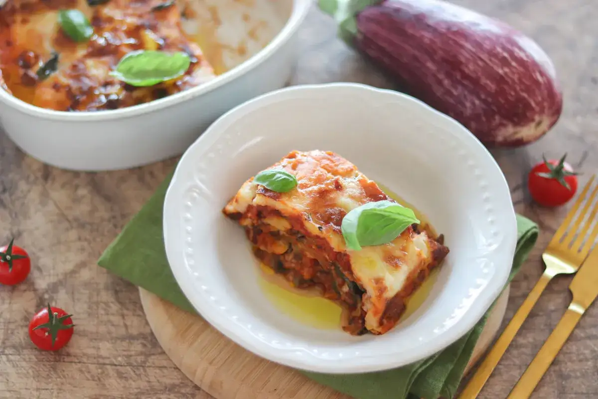 Una fetta di pasticcio di melanzane fumante, con formaggio fuso e basilico fresco, pronta per essere gustata.