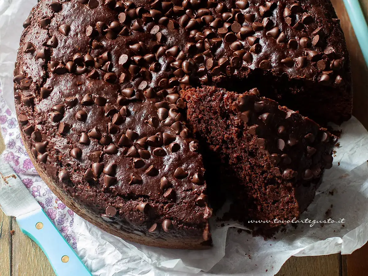 Torta al cioccolato soffice e golosa, ricca di gocce, perfetta per chi cerca dolci senza uova. Una fetta mostra la sua morbidezza.