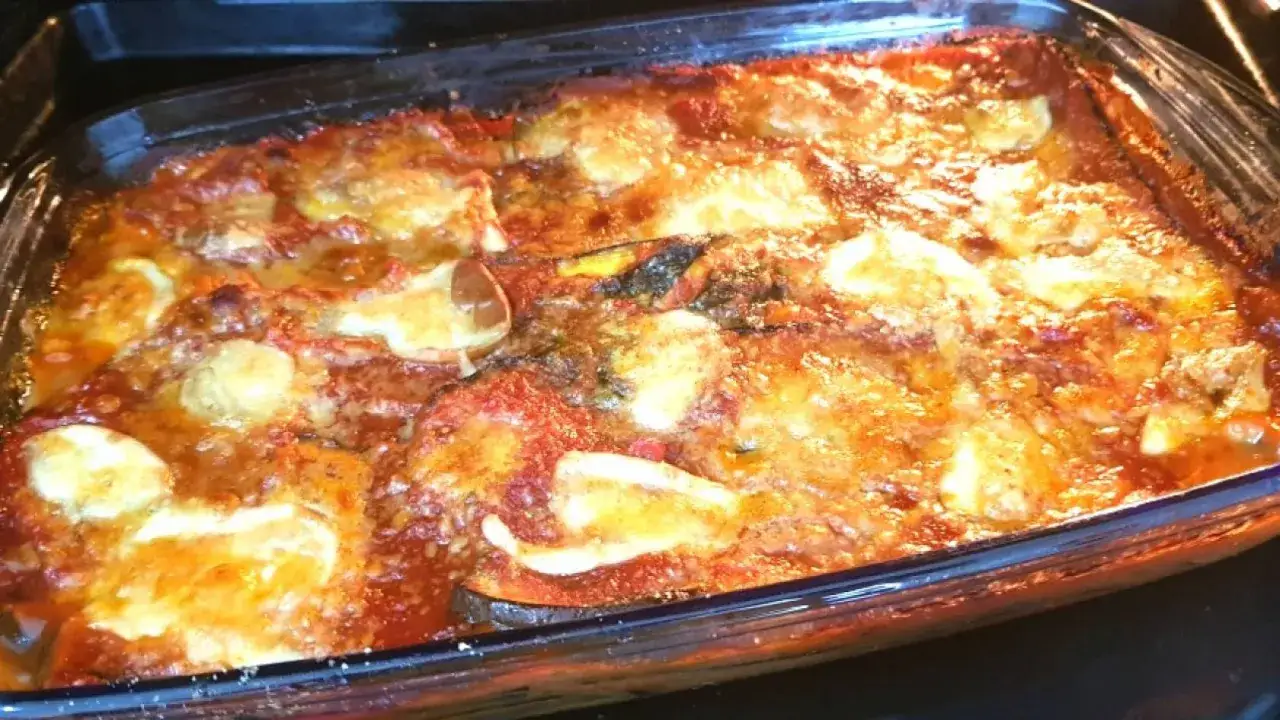 Parmigiana di melanzane grigliate appena sfornata, dorata e filante, in una teglia di vetro.