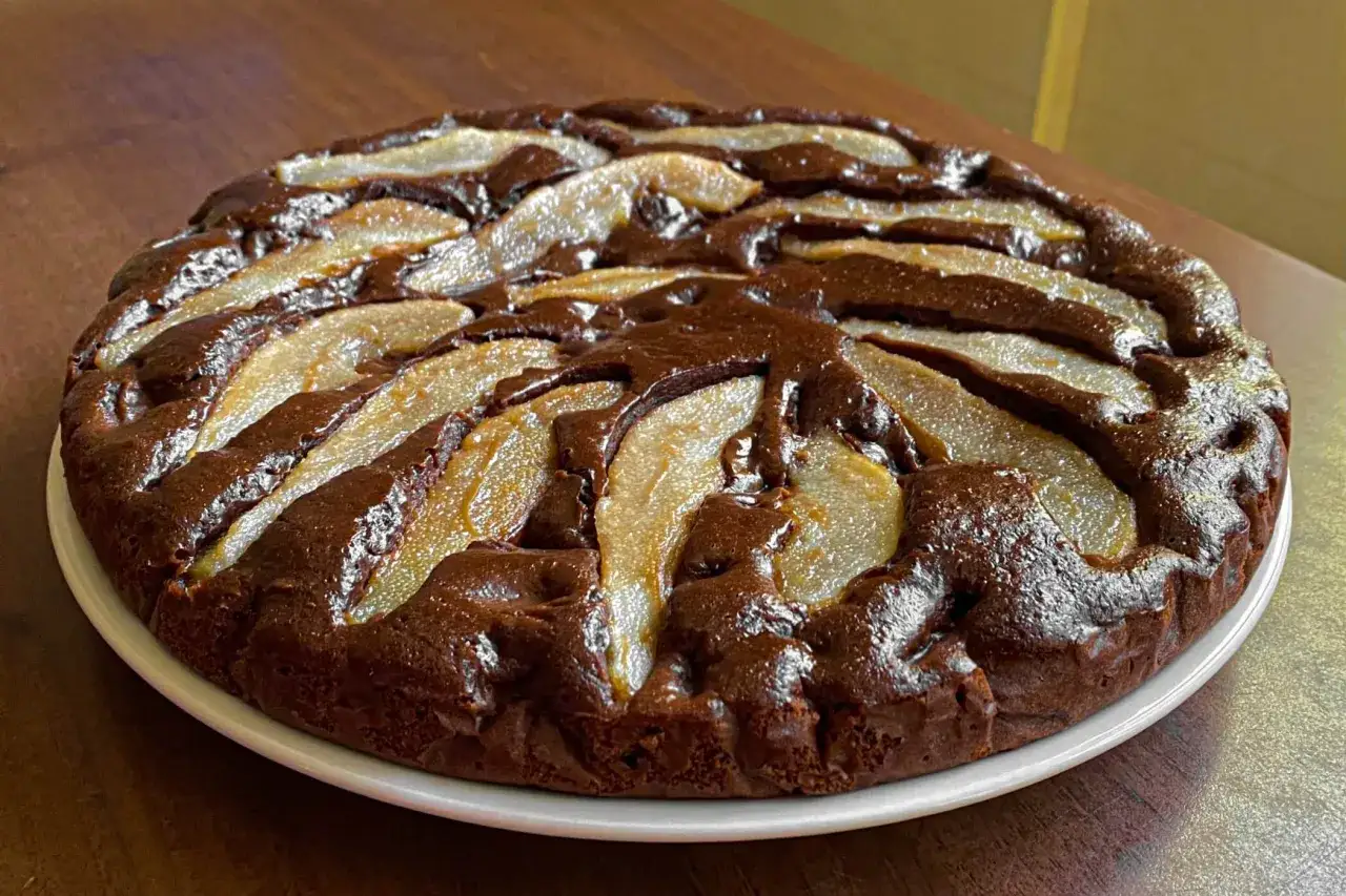 Torta pere e cioccolato, con fette di pera caramellata disposte a raggiera su una base scura e umida.