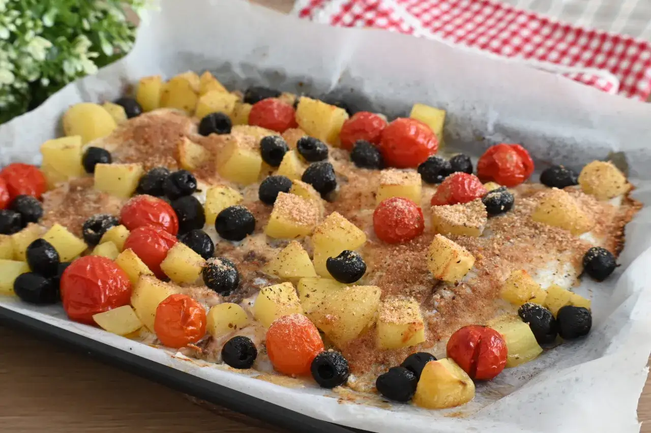 Orata al forno con patate, pomodorini e olive nere, un piatto saporito e colorato, pronto per essere gustato.