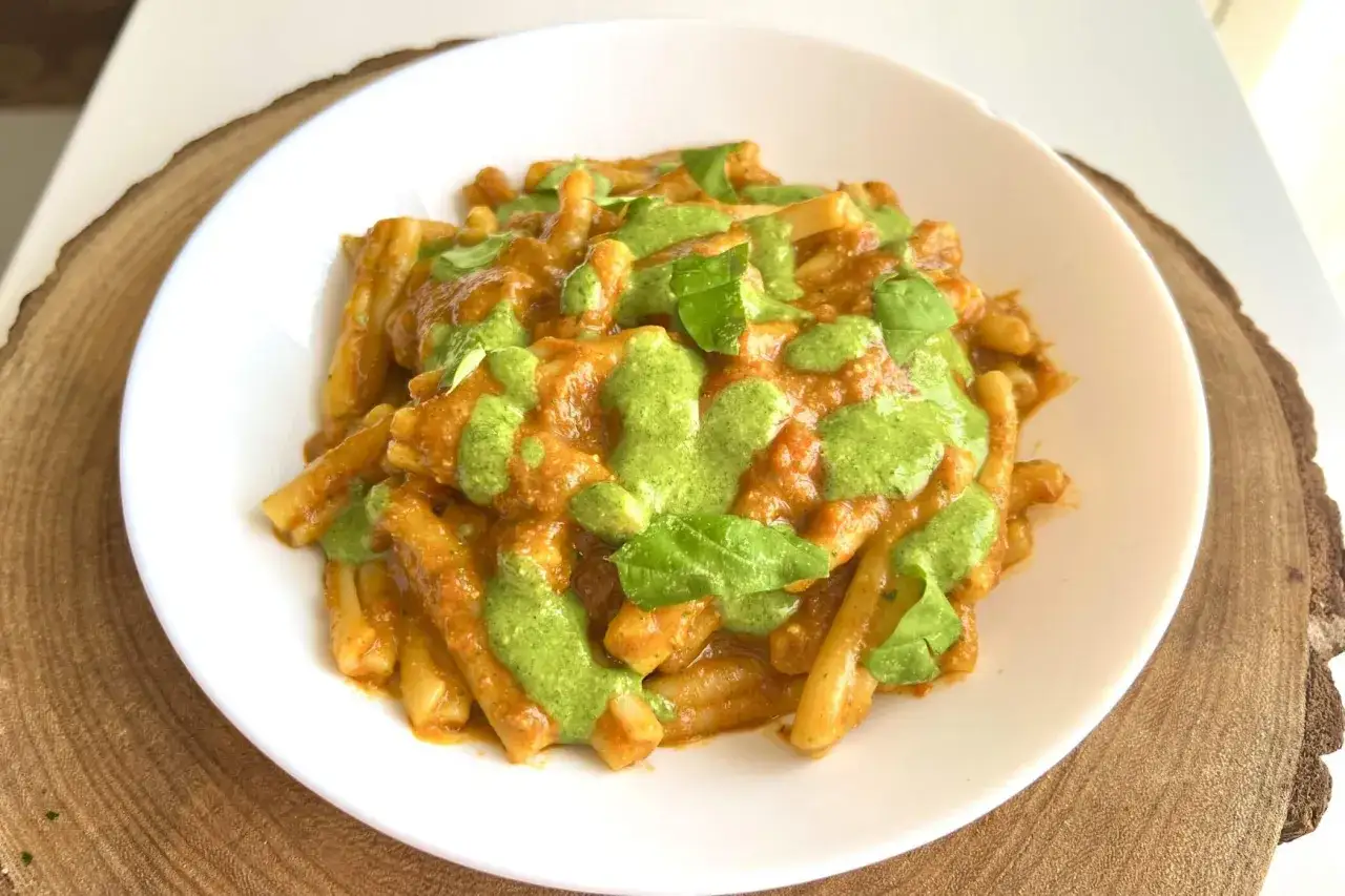 Un piatto di pasta alla Portofino, con un sugo rosso e un pesto verde brillante, guarnito con foglie di basilico fresco.