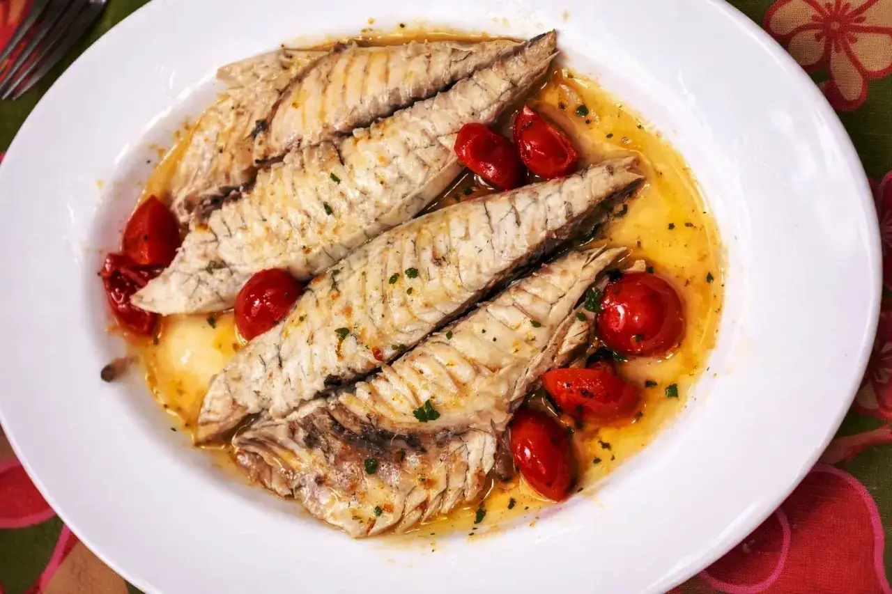 Orata all'acqua pazza, con pomodorini succosi e prezzemolo tritato, servita su un piatto bianco.