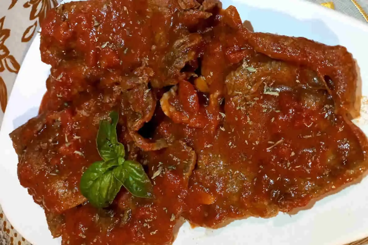 Fette di carne alla pizzaiola, ricoperte da un sugo rosso e profumato, guarnite con basilico fresco.