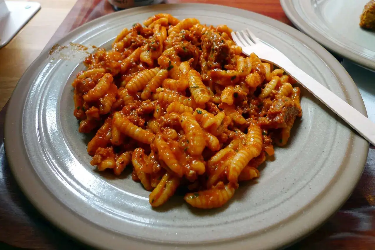 Un piatto di gnocchetti alla campidanese, conditi con un ricco sugo di salsiccia e pomodoro, pronti per essere gustati.