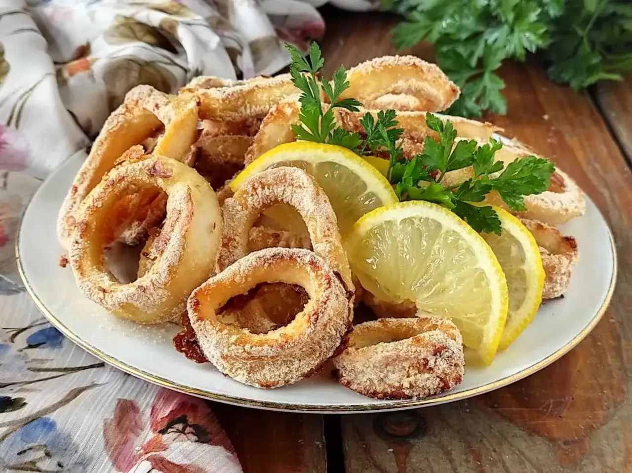 Anelli di calamari al forno dorati e croccanti, guarniti con spicchi di limone fresco e prezzemolo.