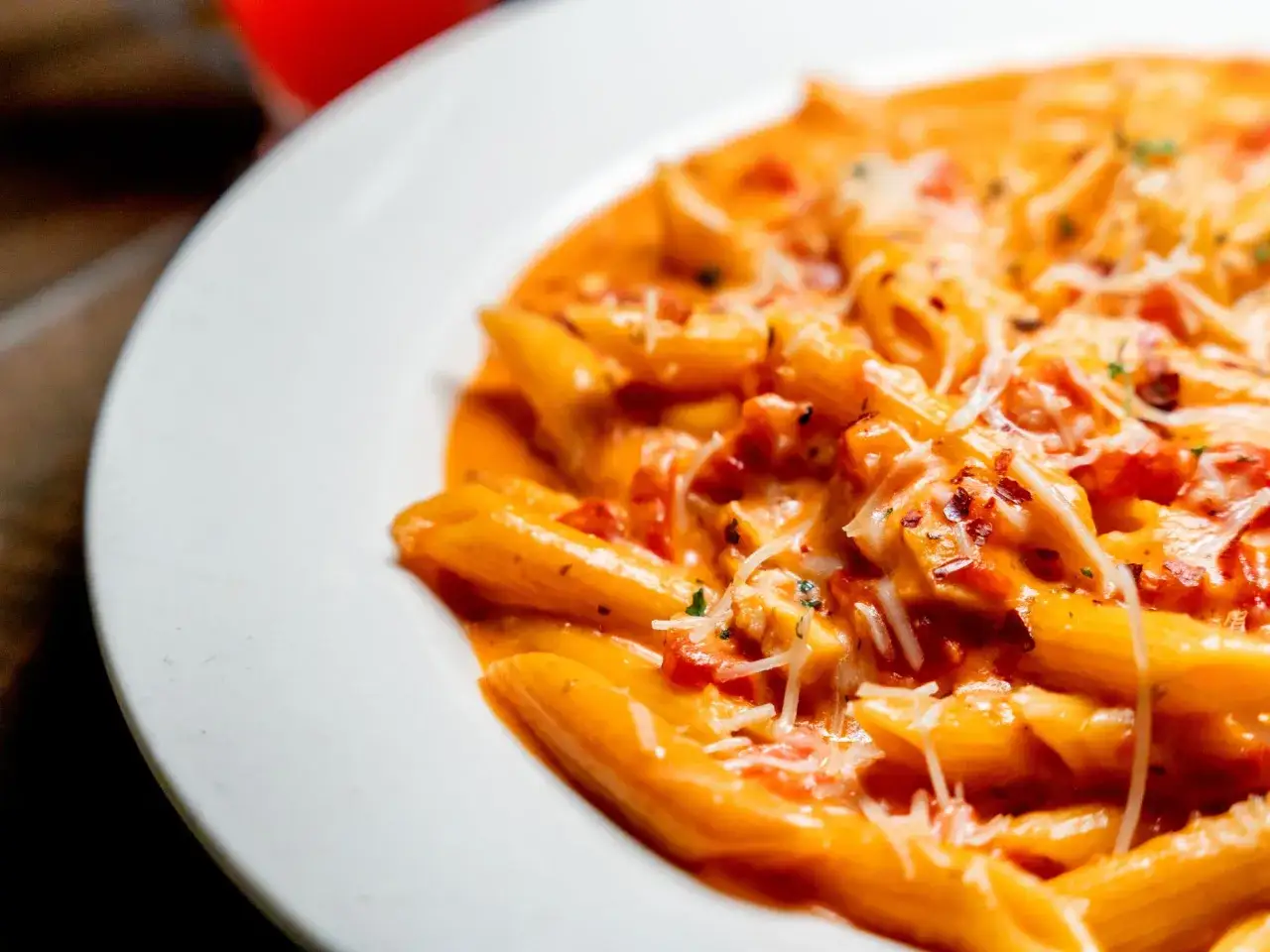 Piatto di penne al baffo cremose, condite con pomodoro e parmigiano grattugiato, un classico invitante.