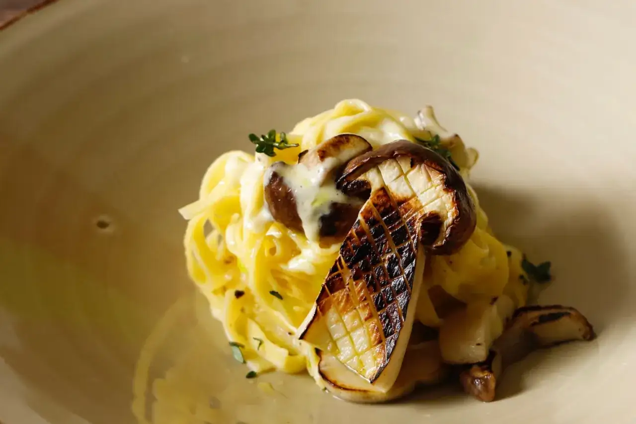 Tagliatelle ai funghi porcini grigliati, condite con una cremosa salsa e guarnite con timo fresco.