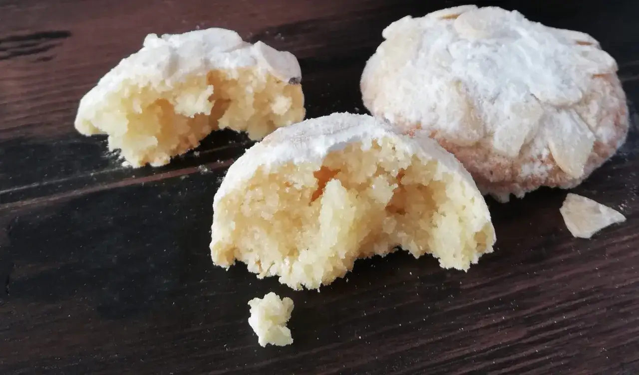 Biscotti alle mandorle cosparsi di zucchero a velo, uno spezzato rivela la loro friabile consistenza.