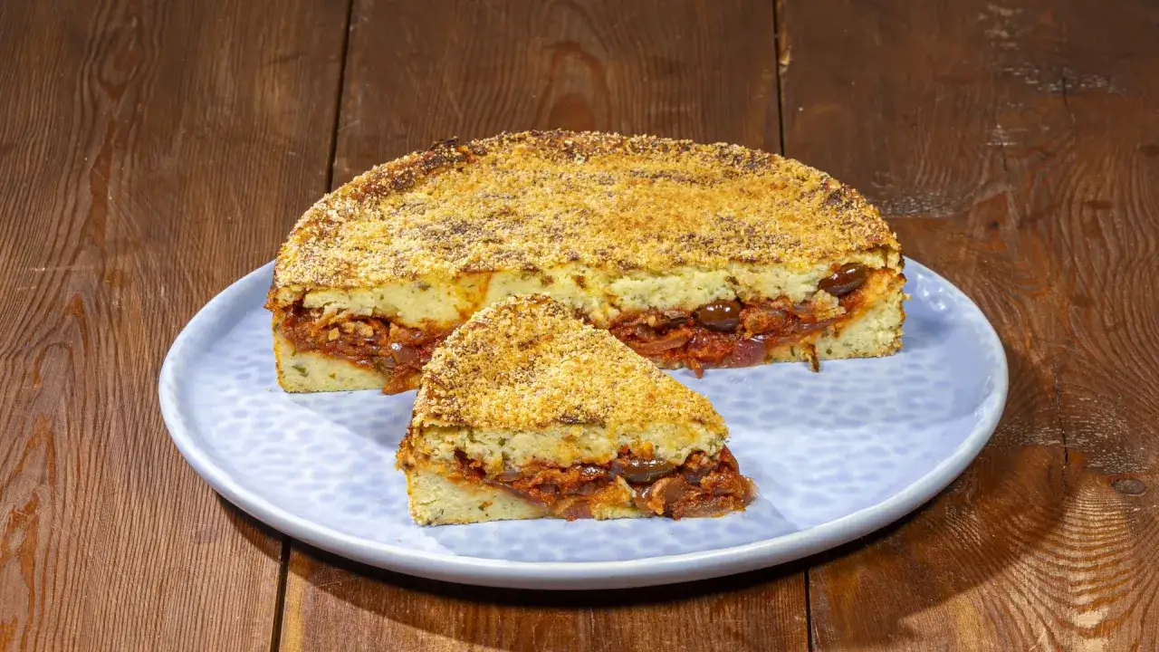 Pitta di patate con ripieno saporito di pomodoro e olive, servita su un piatto azzurro.