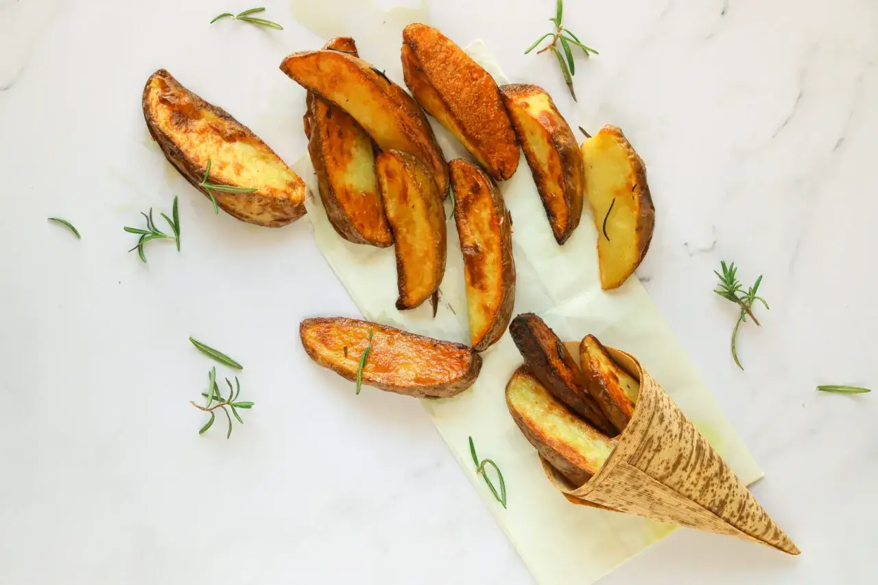 Patate dolci al forno, dorate e croccanti, servite con rametti di rosmarino su carta da forno e in un cono di bamb&ugrave;.