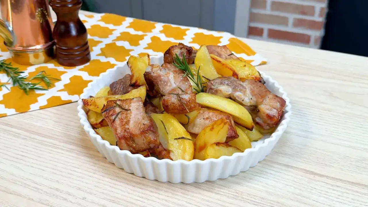 Costine al forno succulente con patate dorate, guarnite con rosmarino fresco. Un piatto invitante e saporito.