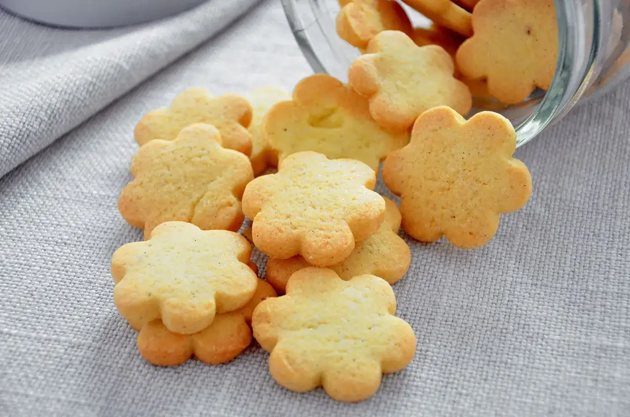 Deliziosi biscotti al burro a forma di fiore, sparsi su una tovaglia grigia.
