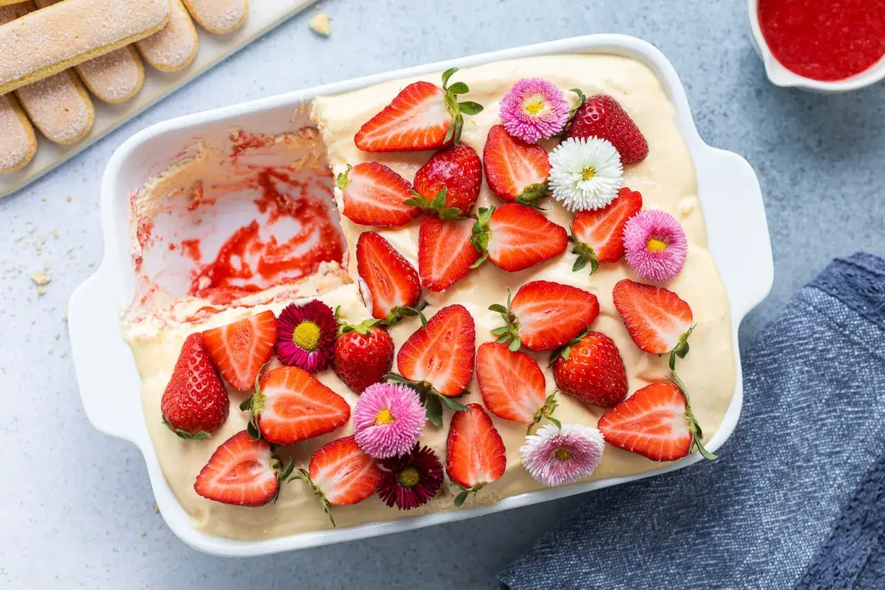 Un invitante tiramisù alle fragole, decorato con fragole fresche e fiori colorati, pronto per essere gustato.