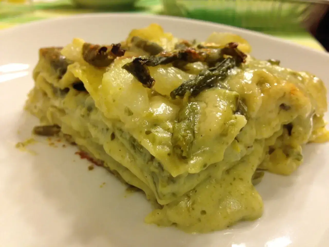 Una fetta di lasagne al pesto, ricca e cremosa, con verdure verdi e formaggio fuso.
