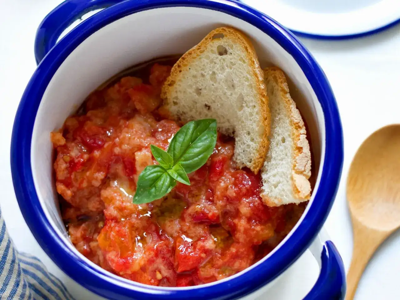 Pappa al pomodoro in una ciotola blu, guarnita con pane tostato e basilico fresco. Un piatto estivo che sa di casa.