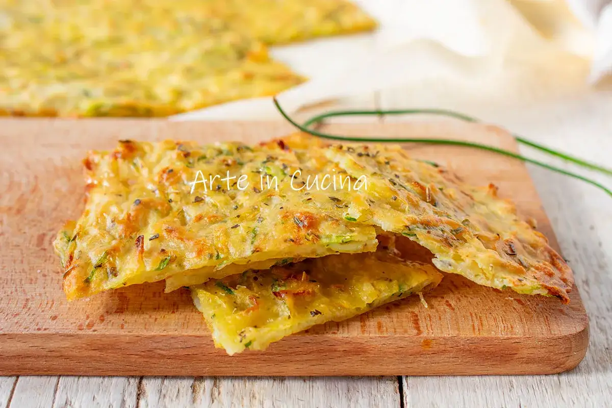 Schiacciata di zucchine dorata e croccante, tagliata a fette su un tagliere di legno, con erbe aromatiche e un filo d'erba cipollina.