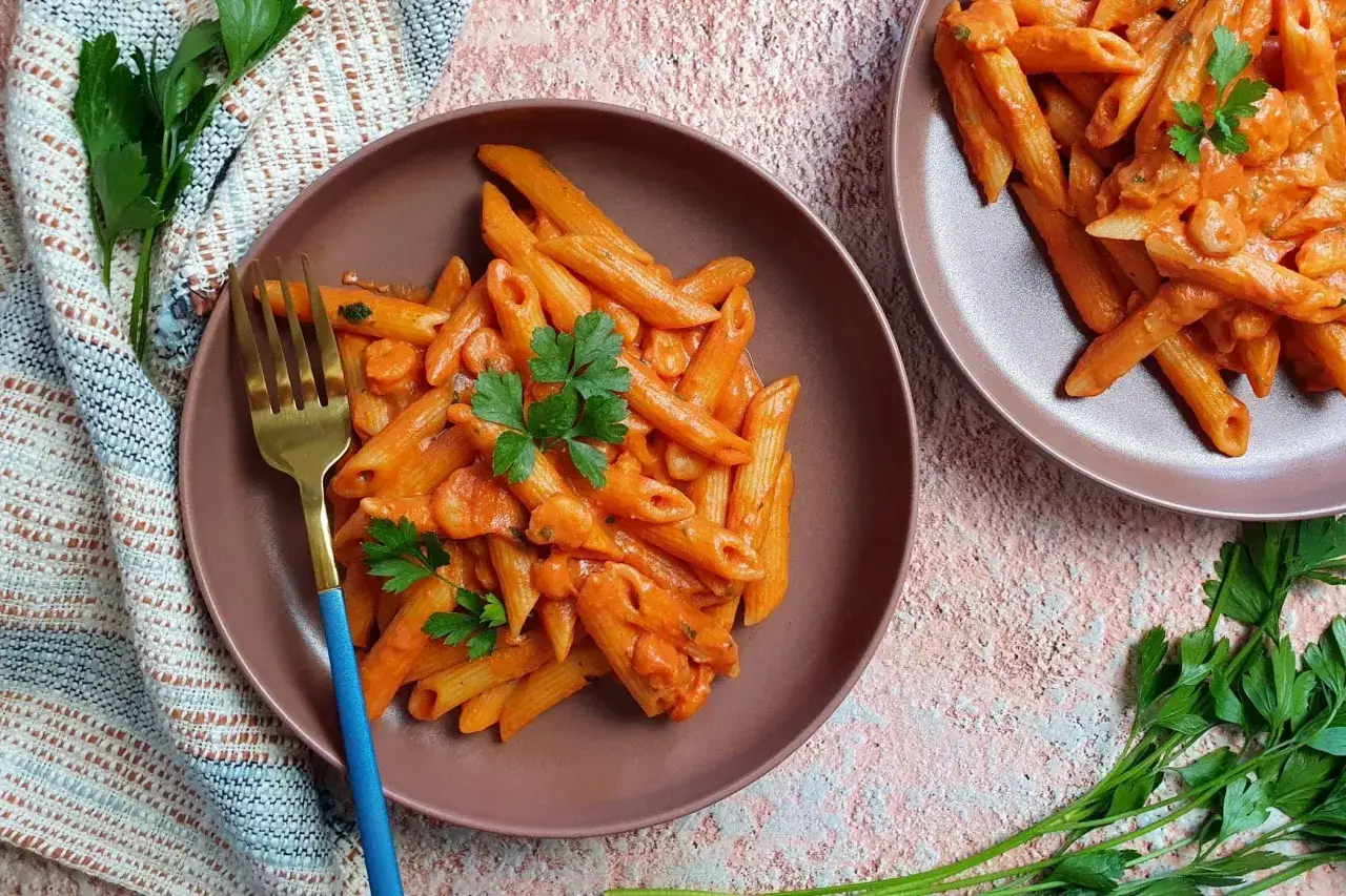 Piatto di penne alla vodka cremose, guarnite con prezzemolo fresco. Una forchetta dorata con manico blu è appoggiata sul piatto.