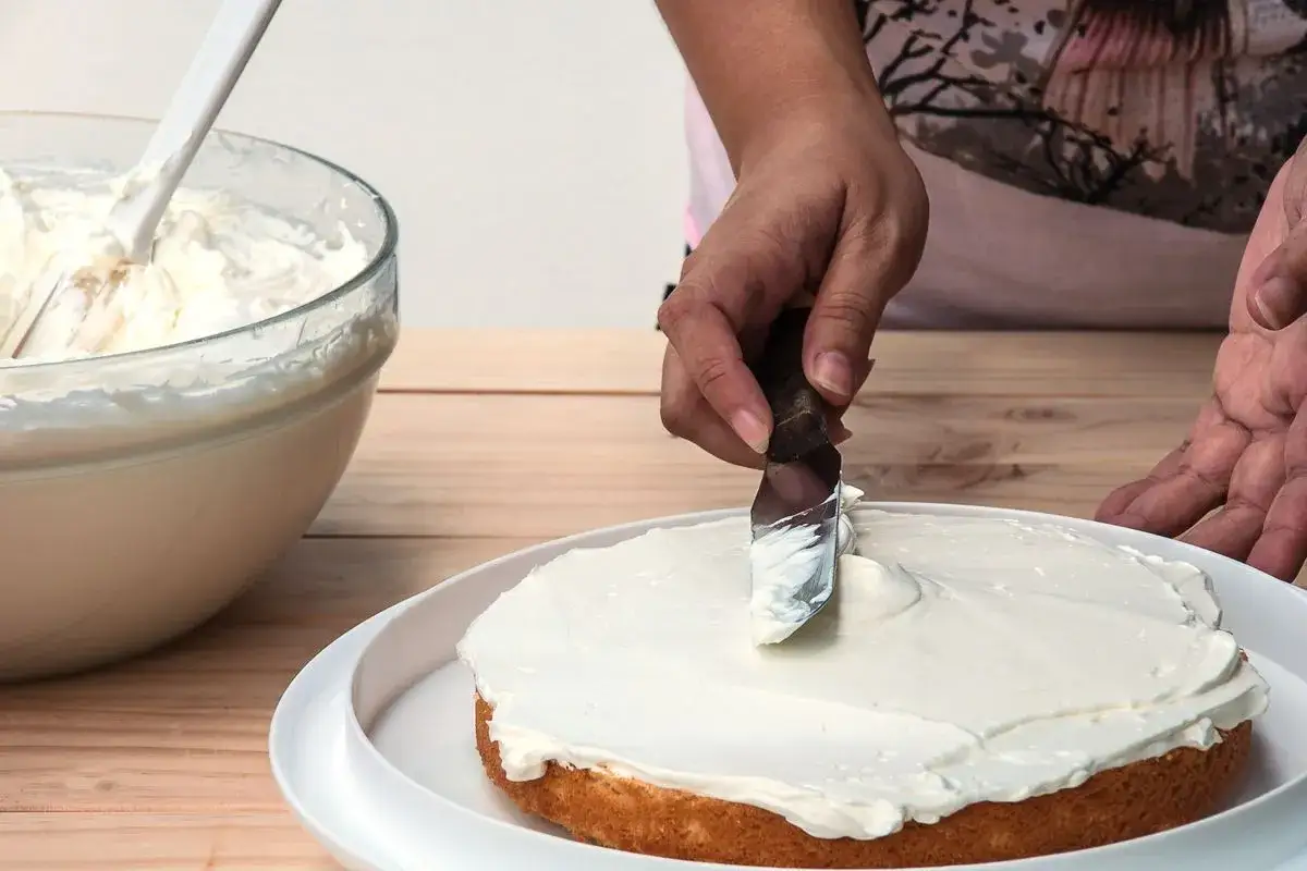 Mani esperte stendono una soffice crema al burro su una torta.