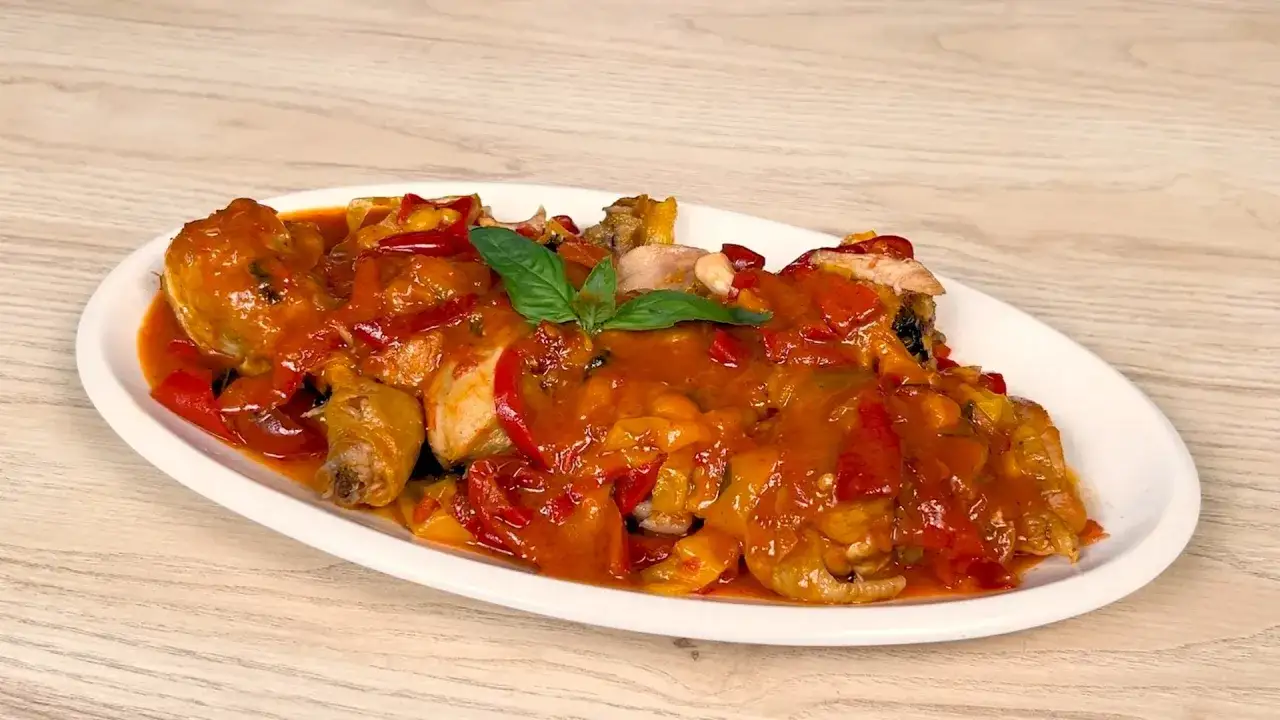 Pollo alla romana succulento, con peperoni rossi e gialli, su un piatto bianco.