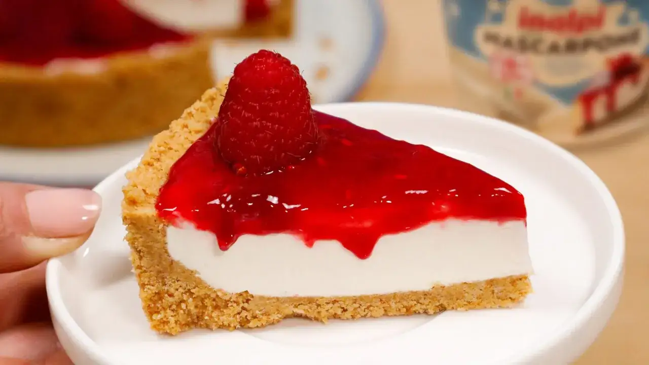 Una fetta di cheesecake con mascarpone, base croccante, ripieno cremoso e topping ai lamponi, guarnita con un lampone fresco.