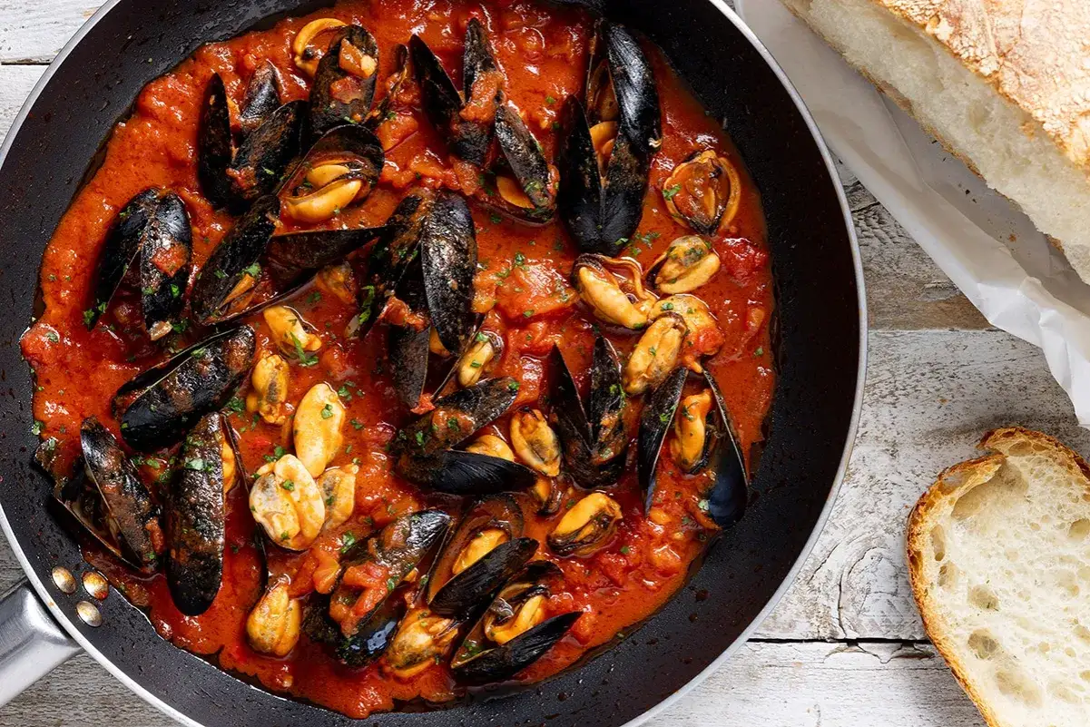 Cozze alla tarantina in padella, con pomodoro e pane fresco. Un piatto succulento pronto da gustare.