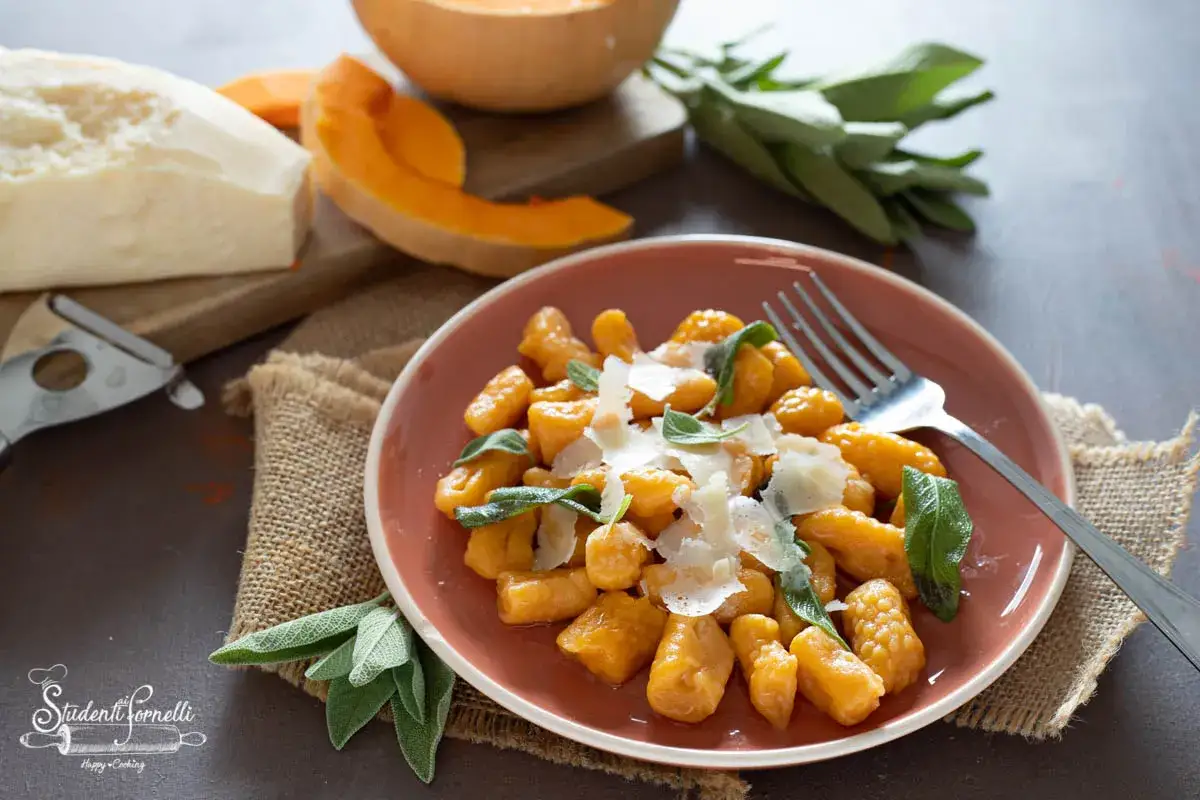 Gnocchi di zucca dorati, guarniti con salvia fresca e scaglie di parmigiano, pronti per essere gustati.