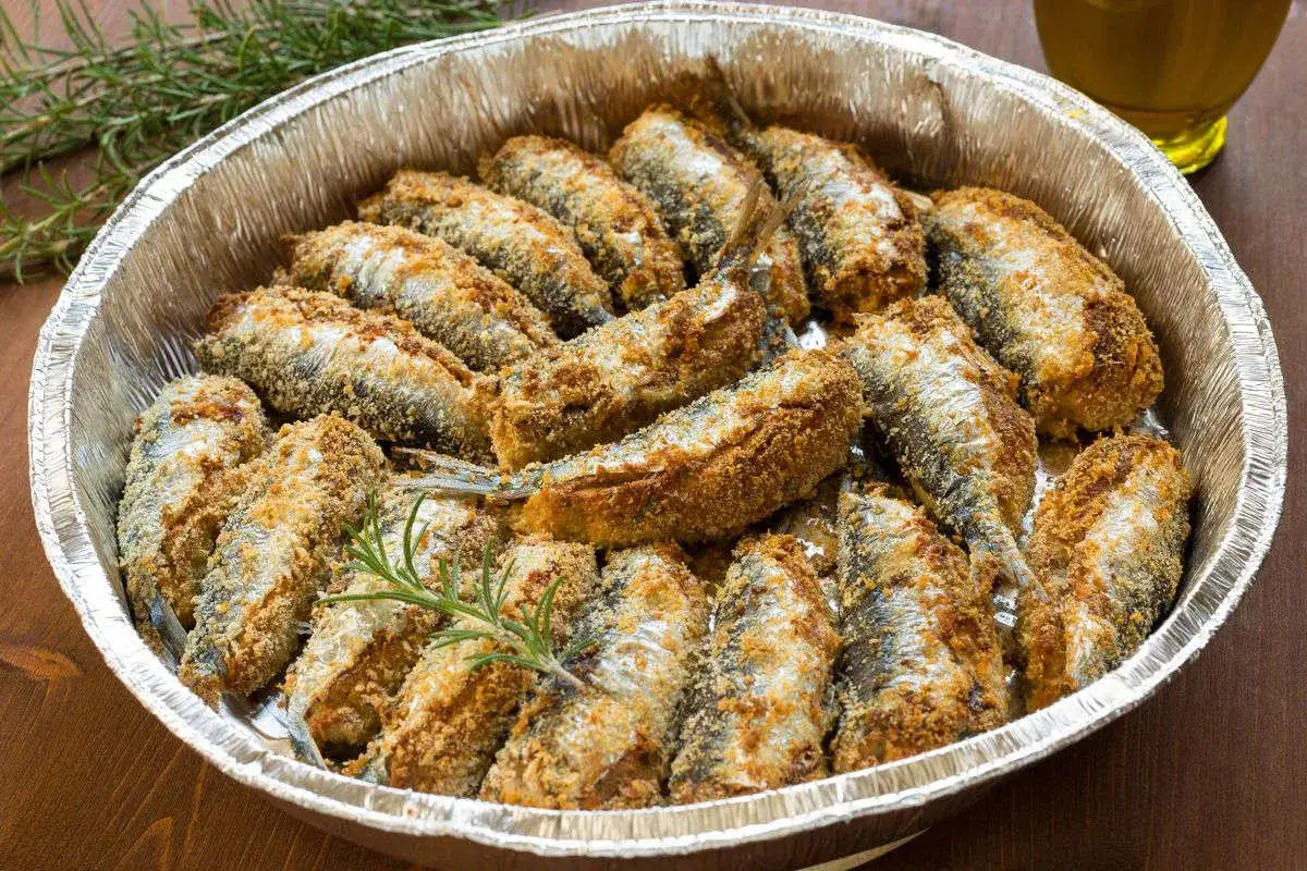 Sardine al forno dorate e croccanti, disposte in una teglia d'alluminio con rametti di rosmarino.