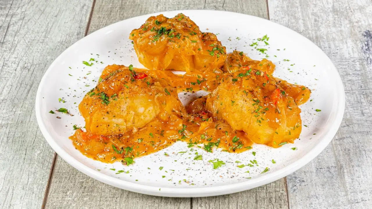 Pezzi di merluzzo in umido, cotti lentamente in un sugo saporito con cipolle e peperoncino, guarniti con prezzemolo fresco.