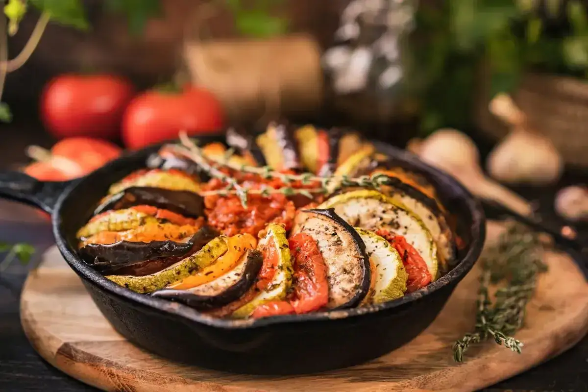 Ratatouille in padella, un piatto colorato con fette alternate di melanzane, zucchine e pomodori, condito con erbe aromatiche.