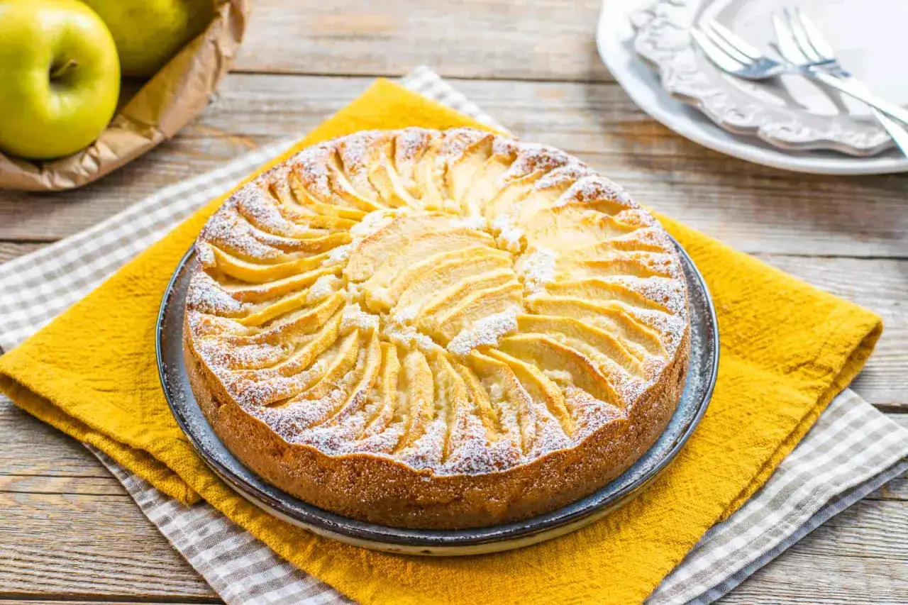 Una deliziosa torta di mele senza zucchero, decorata con fettine di mela e spolverata di zucchero a velo, su un tavolo di legno.