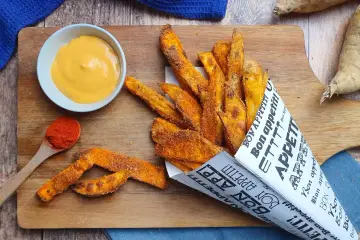 Patate dolci al forno croccanti, servite in un cono di carta con una salsa cremosa e paprika.