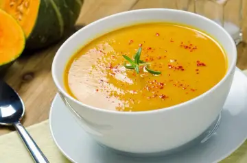 Una cremosa vellutata di zucca, guarnita con rosmarino e paprika, pronta per essere gustata.