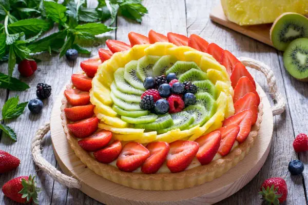 Una colorata crostata di frutta, con fragole, kiwi, ananas e frutti di bosco, su un tavolo di legno rustico.