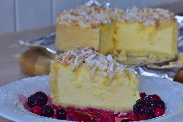 Una fetta di torta di riso cremosa, guarnita con mandorle a lamelle e frutti di bosco, su un piatto bianco.
