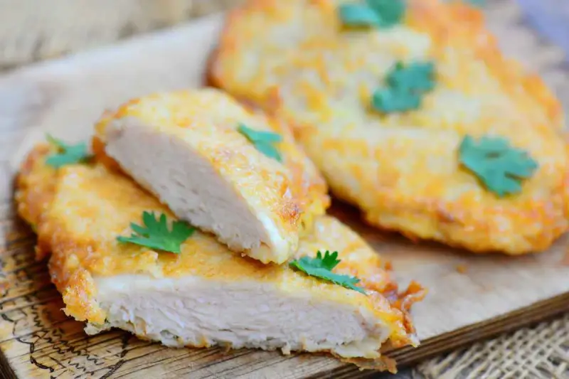 Deliziose cotolette di pollo dorate, tagliate a metà per mostrare la succosa carne bianca, guarnite con prezzemolo fresco.