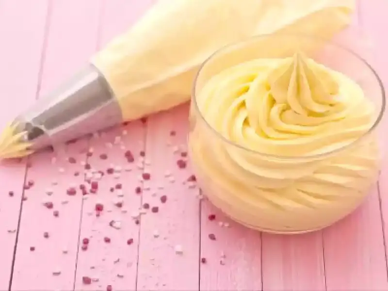 Sac à poche con crema al burro pronta per decorare, accanto a un bicchiere colmo della stessa soffice crema.